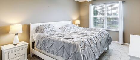Un dormitorio con cama, mesitas de noche, ventilador de techo y una ventana con persianas.