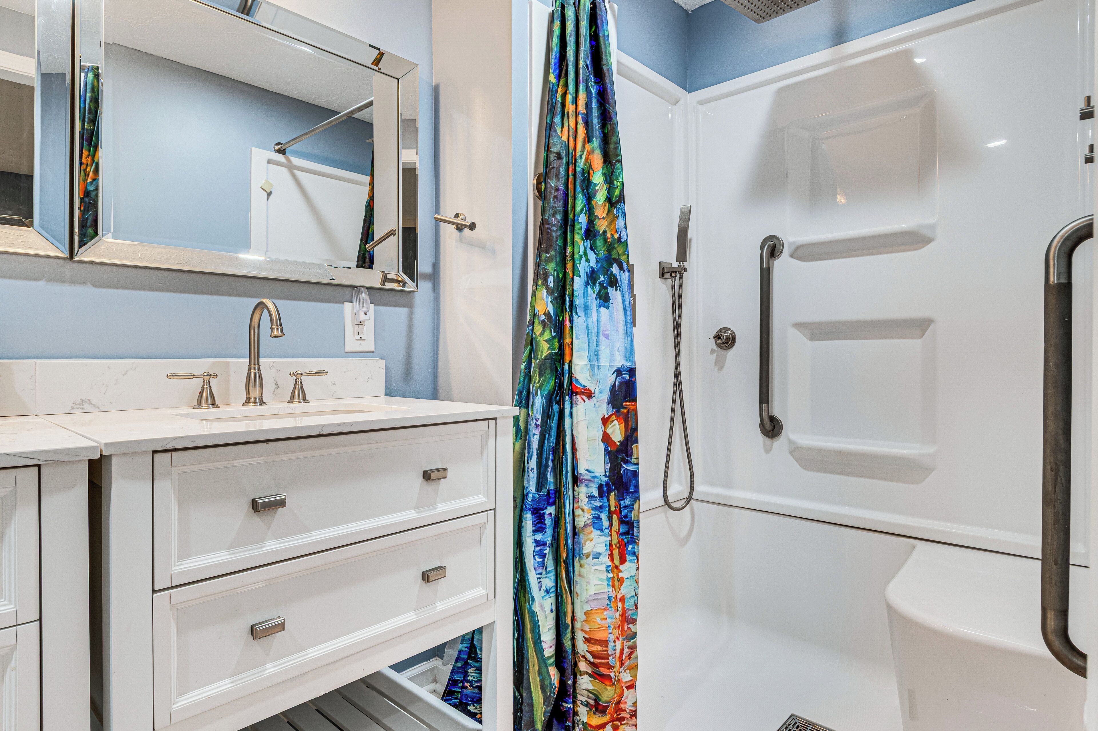 A bathroom with a white vanity, a mirror, a shower with a colorful curtain, and a toilet.