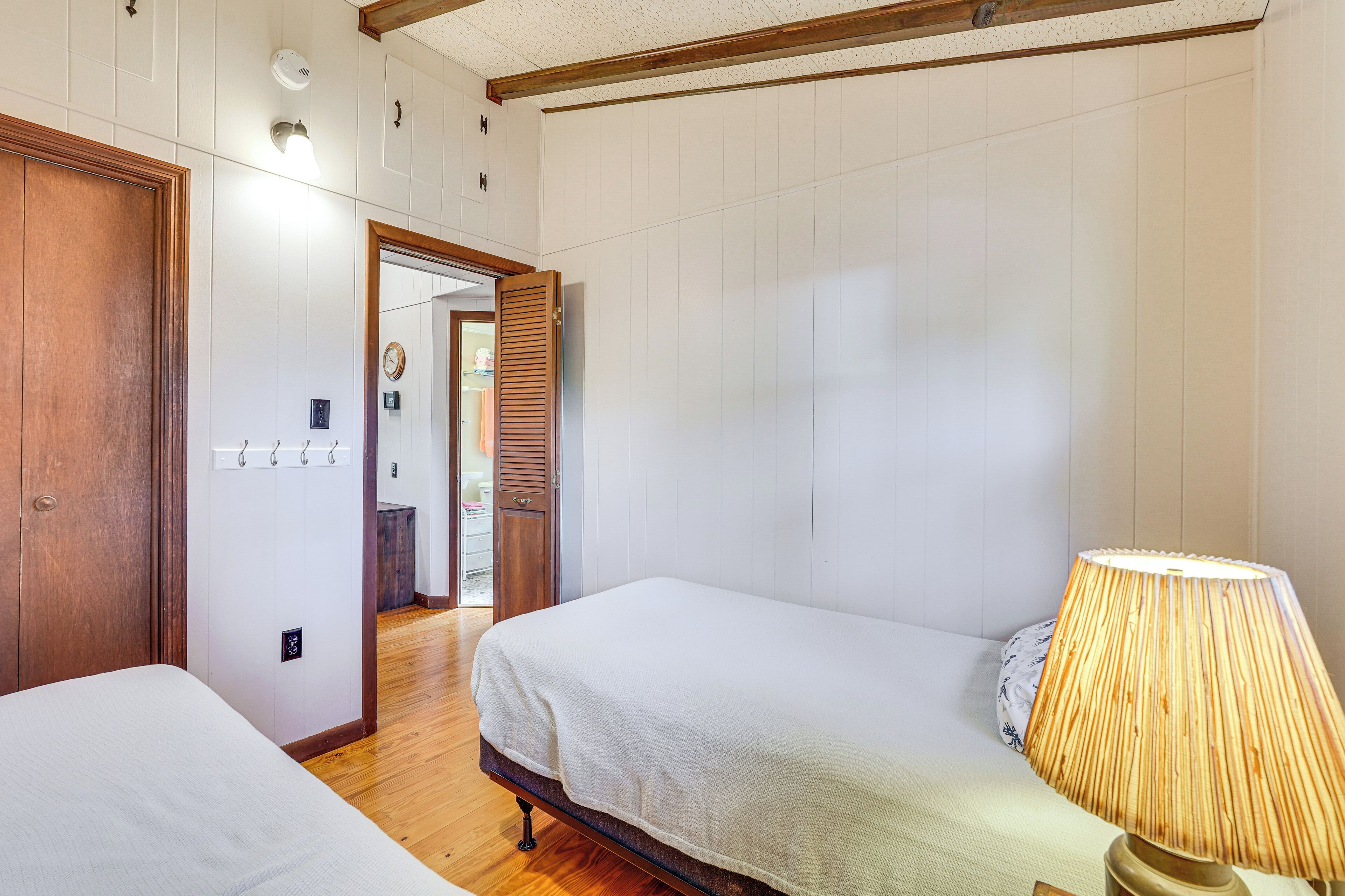 A hotel room with two single beds, a wooden floor, a wall-mounted lamp, and a door leading to a bathroom.