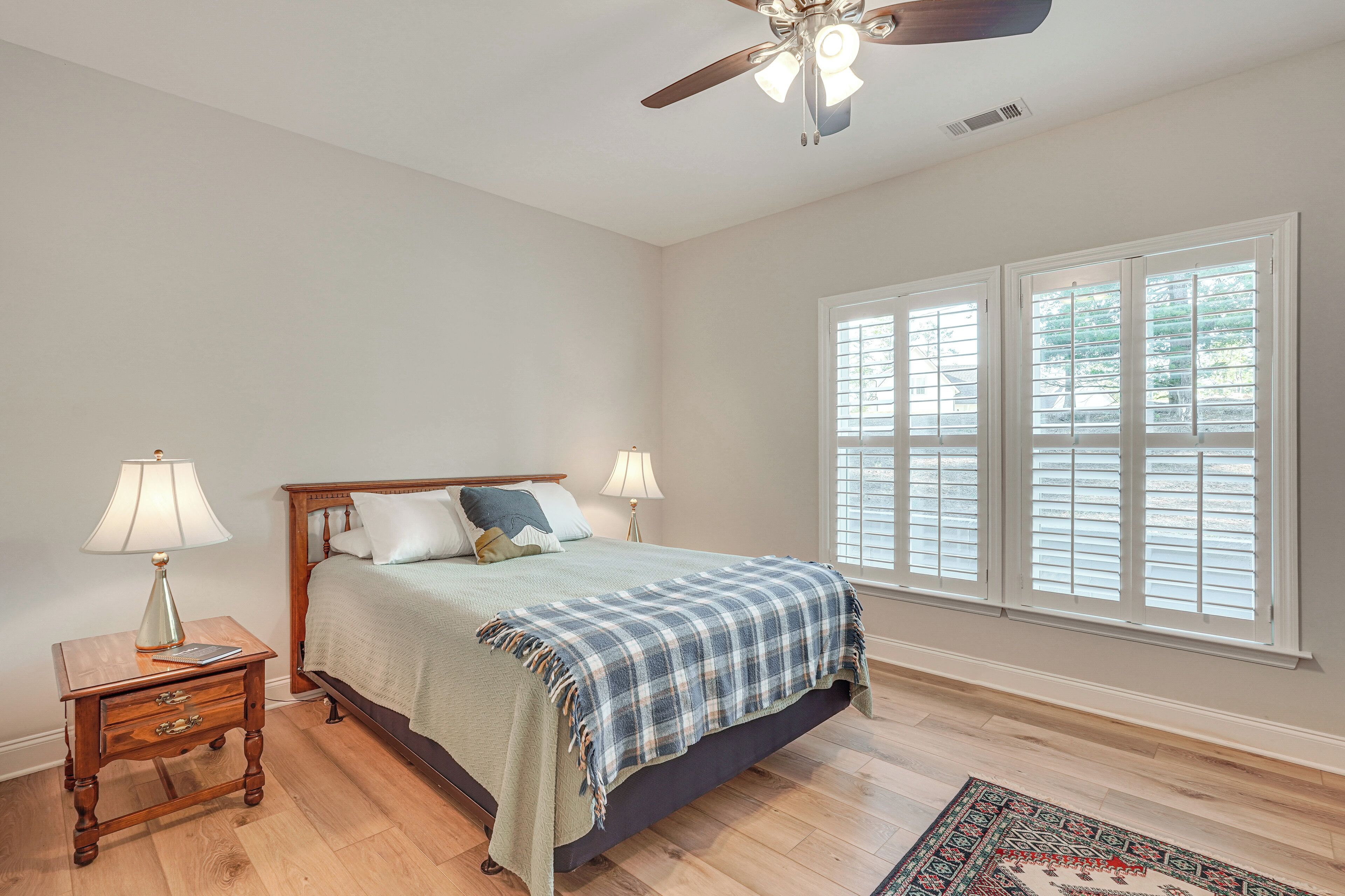 A bedroom with a bed, nightstand, lamp, and window with blinds.