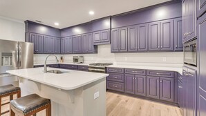A modern kitchen with purple cabinets, a central island with stools, stainless steel appliances, and a white countertop. - Clark's Hill Lake Retreat! Waterfront Home w/ Dock (Modoc)