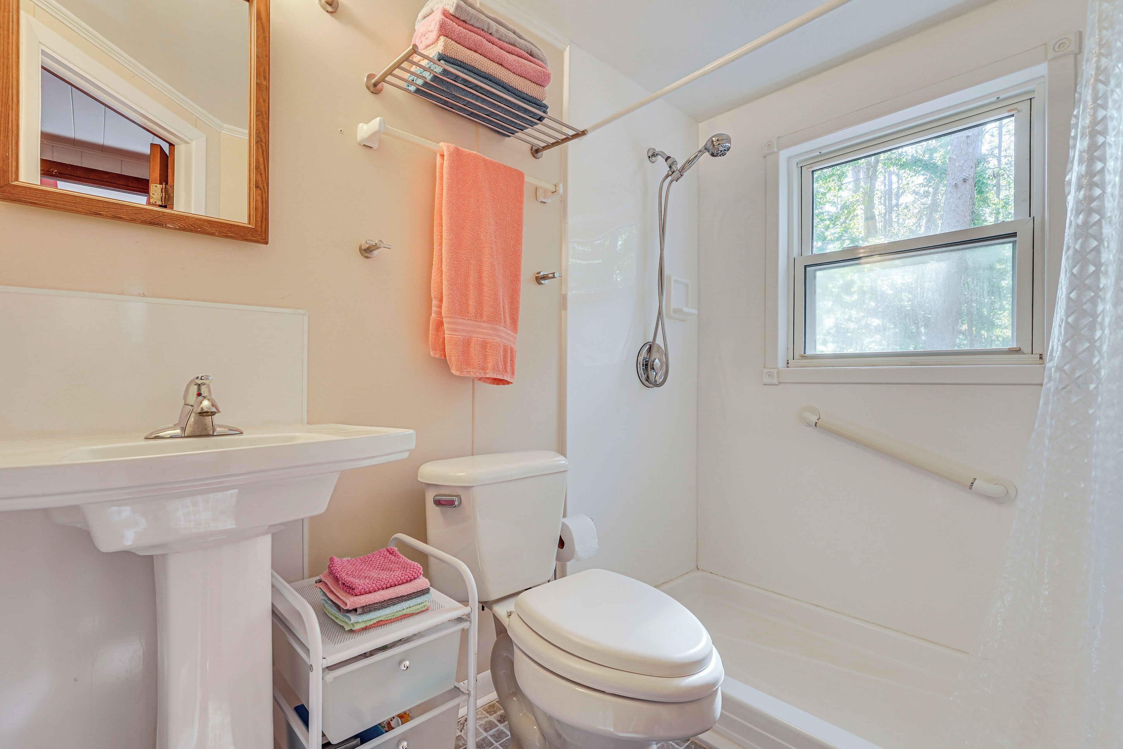 A bathroom with a sink, toilet, and shower. There is a window with a view of trees.