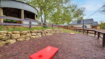 A covered outdoor area with a red disc golf target, stone wall, wooden fence, and a building with a metal roof.