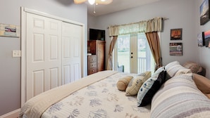 Une chambre à coucher avec un lit, un ventilateur de plafond, une commode et une fenêtre avec des rideaux.