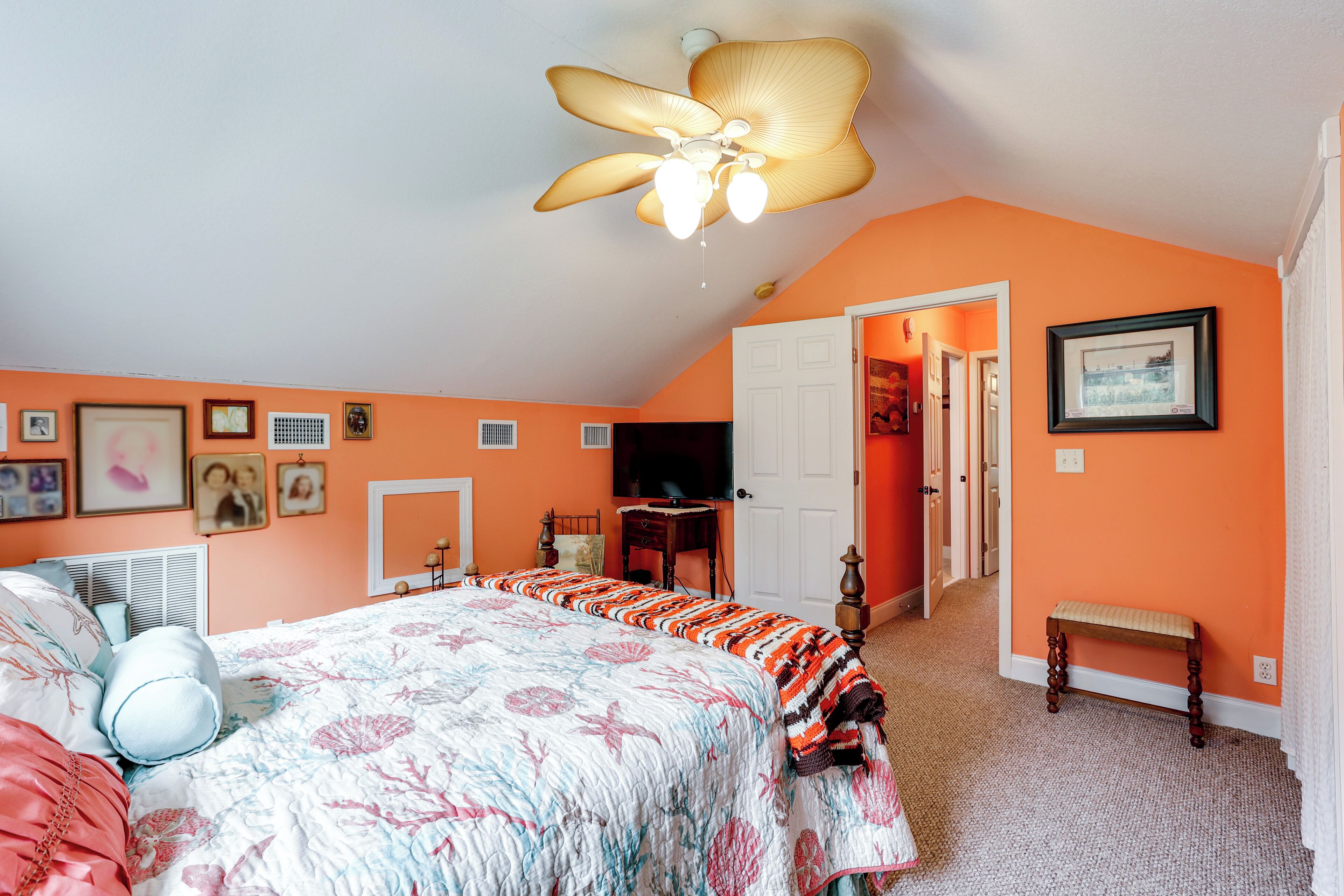 Une chambre avec un grand lit, un ventilateur de plafond et une porte donnant sur une autre pièce.
