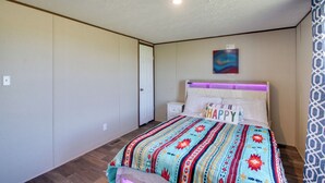 Una camera da letto con un letto, un comodino, una porta e un quadro appeso al muro.