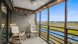 A porch with two rocking chairs, a ceiling fan, and a view of a water body. - Walkin on Sunshine! Marshside Inn 309 (Murrells Inlet)