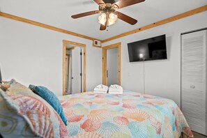Une chambre à coucher comprenant un lit, un ventilateur de plafond, une télévision et une armoire.