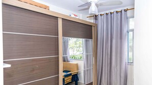 Een kamer met een schuifkasten, een plafondventilator, een raam met gordijnen en een klein tafeltje met stoel.