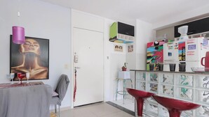 Une cuisine moderne avec un coin repas, un réfrigérateur décoré d’aimants et un tableau accroché au mur.
