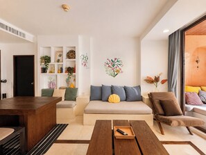 A modern living room with a sofa, a wooden coffee table, a side table, a bookshelf, and a door. - Hua Hin Beach Front Condo - Family Suite Room at Las Tortugas (Tambon Nong Kae)