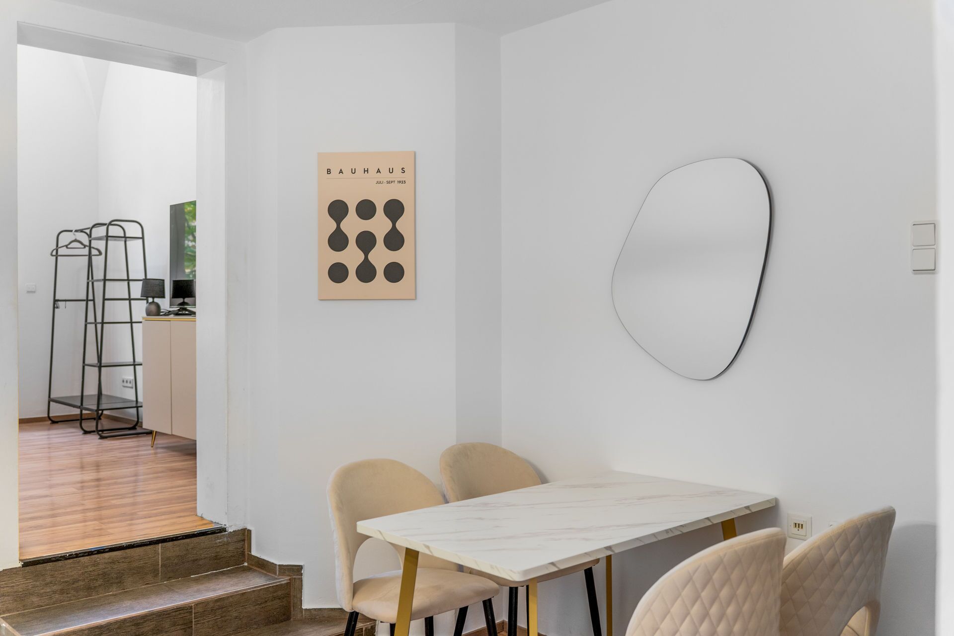 Ein moderner Essbereich mit einem Marmortisch, gepolsterten Stühlen, einem schwarzen Kleiderständer und einem Bauhaus-Poster an der Wand.