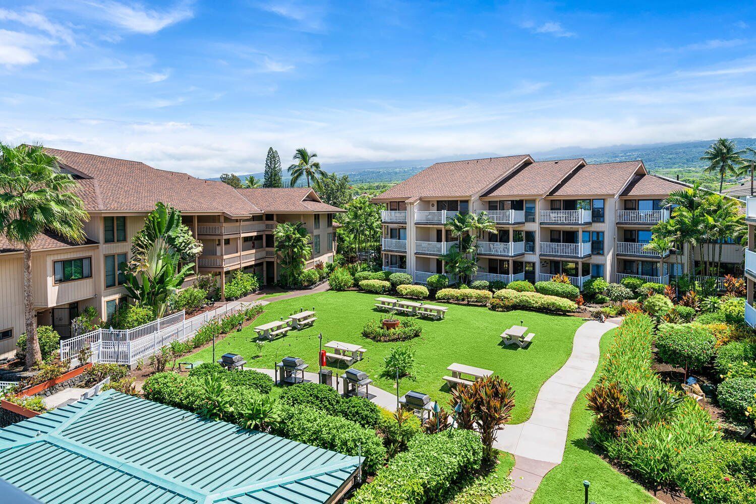 Un hotel con edificios de varios pisos, césped bien cuidado, mesas de picnic y una vista despejada del paisaje circundante.