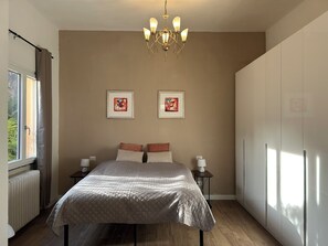 A bedroom with a bed, two framed artworks, a chandelier, a radiator, and a wardrobe. - Villa Giulia - Vista Verde at 5 min from  the lake (Porto Valtravaglia)