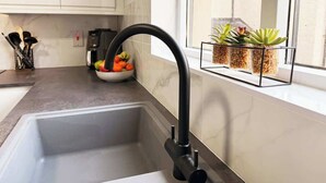Una cocina con un grifo moderno, un cuenco de fruta y una ventana con plantas.