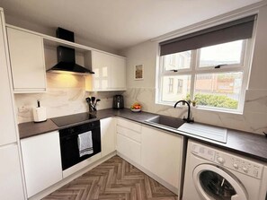 A compact kitchen with a built-in oven, a washing machine, and a window providing natural light.