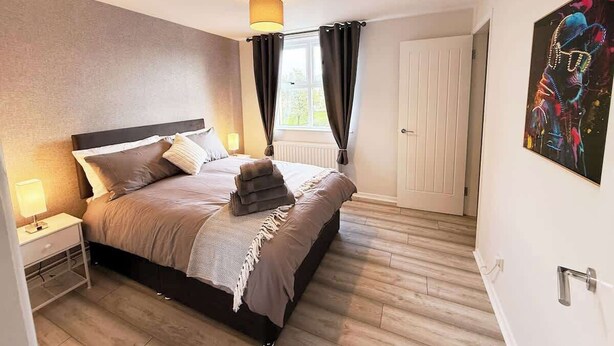 Un dormitorio con cama, mesita de noche, lámpara, cortinas y una puerta.