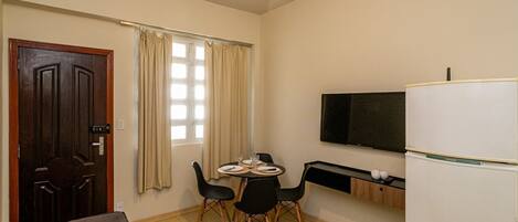 A compact living space with a dining area, a flat-screen TV, a refrigerator, and a ceiling fan.