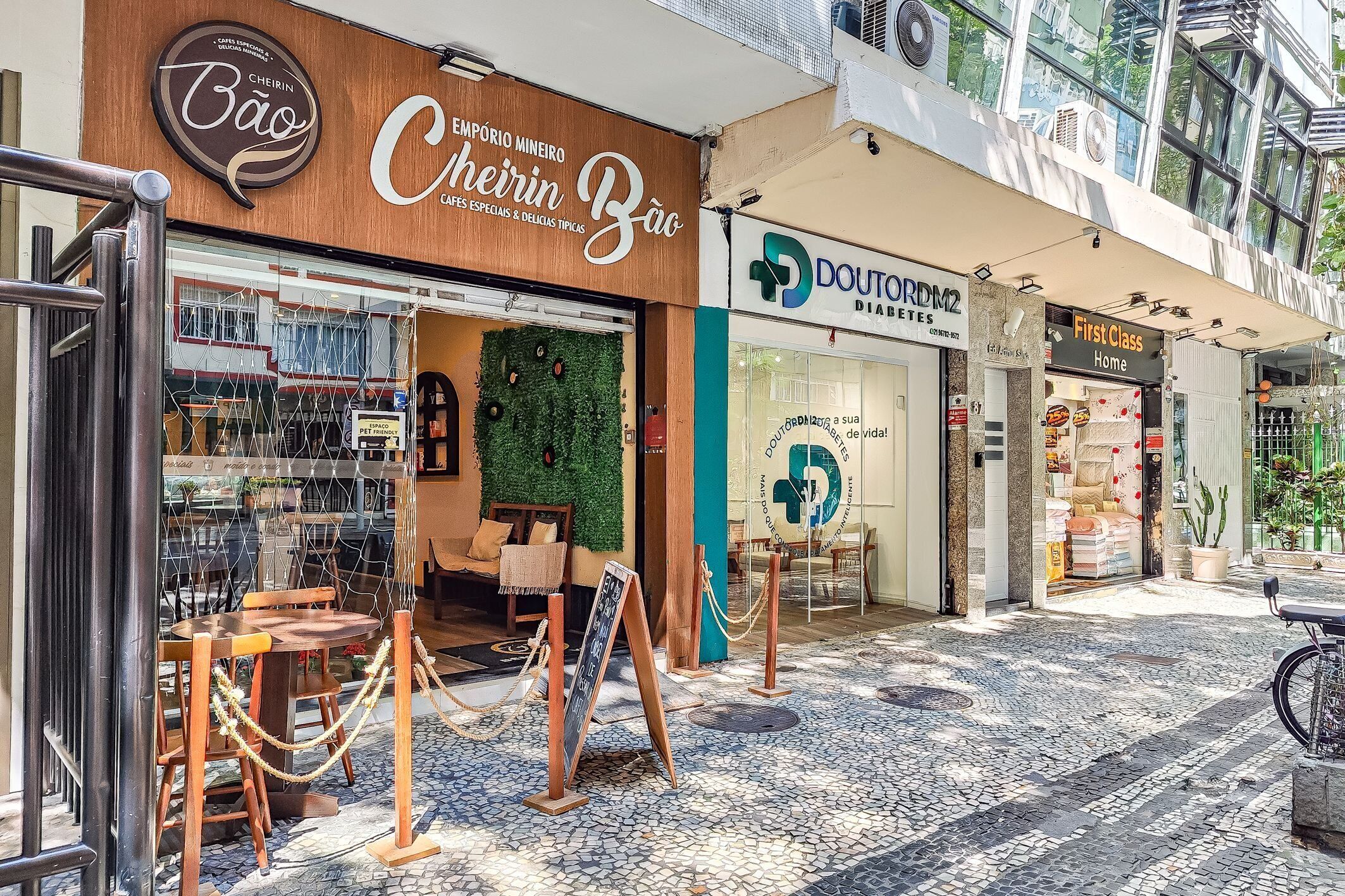 A café with a wooden exterior and a green wall, a pharmacy, and a store with a sign reading 'First Class Home.'