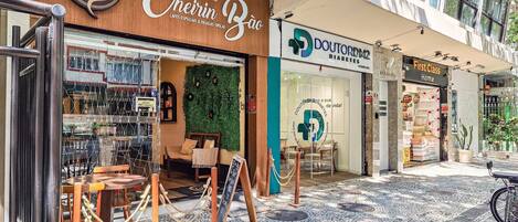 A café with a wooden exterior and a green wall, a pharmacy, and a store with a sign reading 'First Class Home.'