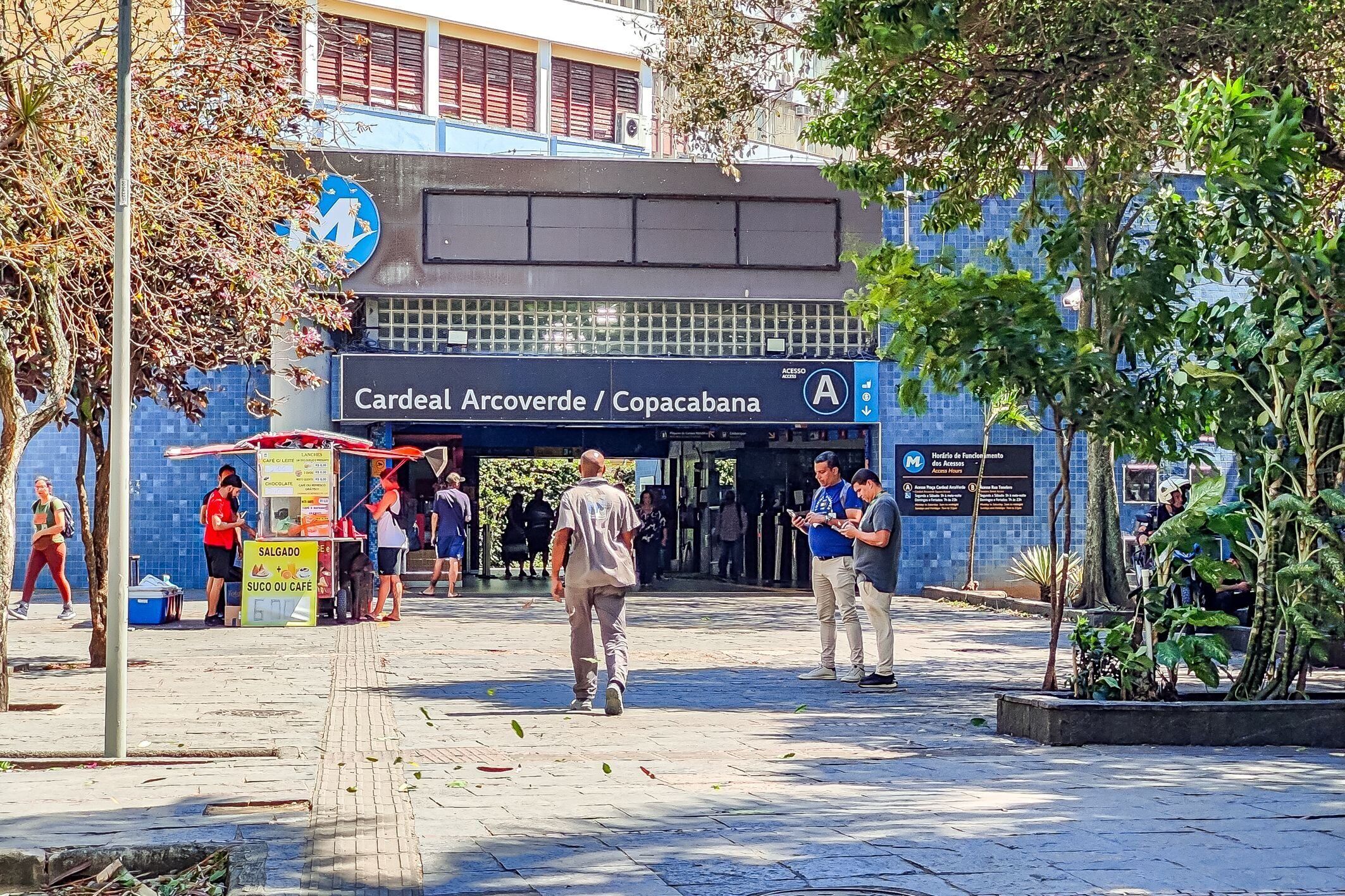 Un espacio al aire libre con un edificio azul, un cartel que dice 'Cardenal Arcoverde / Copacabana' y un quiosco.