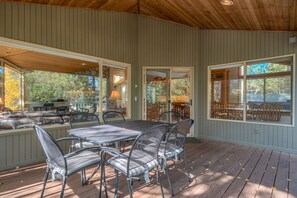 Un patio couvert avec une table et des chaises, une terrasse en bois et de grandes fenêtres.