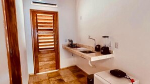 Une cuisine compacte avec un plafond en bois, un évier encastré, un petit réfrigérateur et une porte dotée de stores horizontaux.