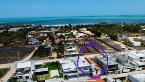 Vue aérienne d’un quartier résidentiel situé sur la côte, avec des maisons modernes, une plage et une vue dégagée sur l’océan.