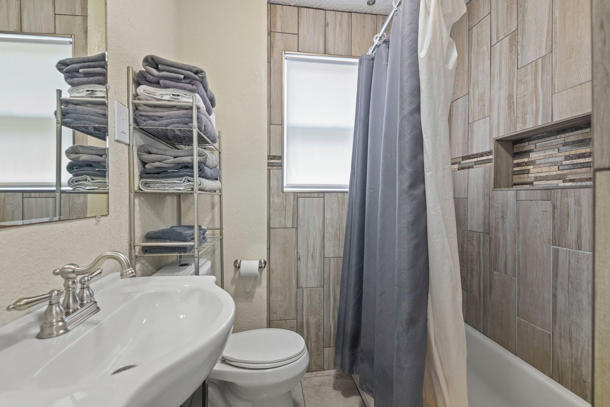 A bathroom with a white sink, toilet, and shower curtain. There are shelves with folded towels.