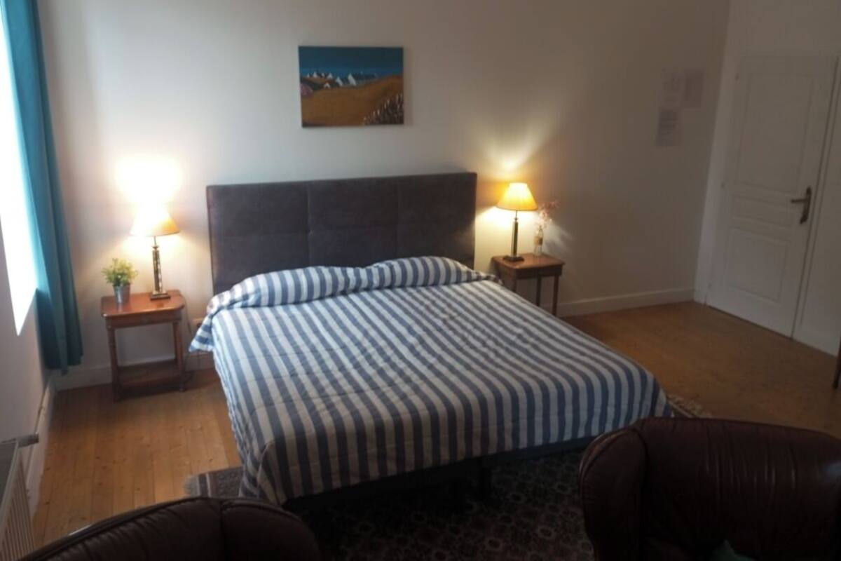Een slaapkamer met een bed, twee bedlampjes, een nachtkastje, een stoel en een deur.