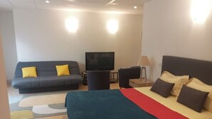 A modern hotel room with a large bed, a sofa, a television, and a lamp.