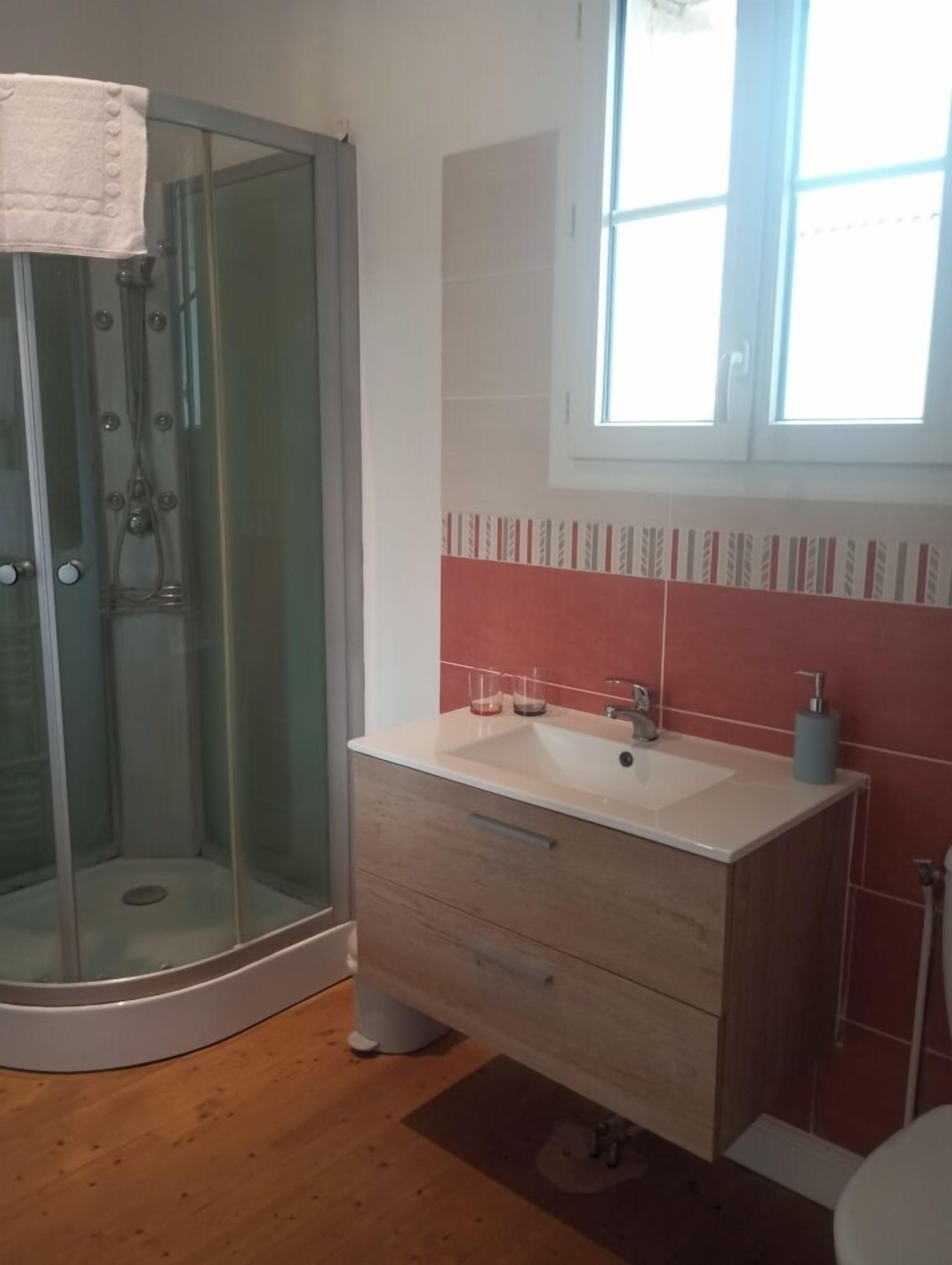 A bathroom with a glass shower enclosure, a sink with a mirror, and a window providing natural light.