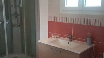 A bathroom with a glass shower enclosure, a sink with a mirror, and a window providing natural light.