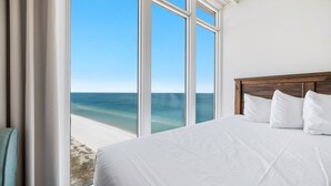 A bedroom with a large window overlooking a beach, a wooden headboard, and white bedding. - Penthouse 4BR, Beachfront!, Lazy River/Slide! (Orange Beach)