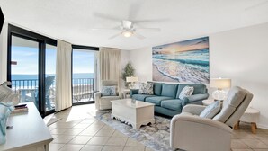 Un soggiorno moderno con vista sull'oceano, una ventola a soffitto e un grande quadro che raffigura la spiaggia.
