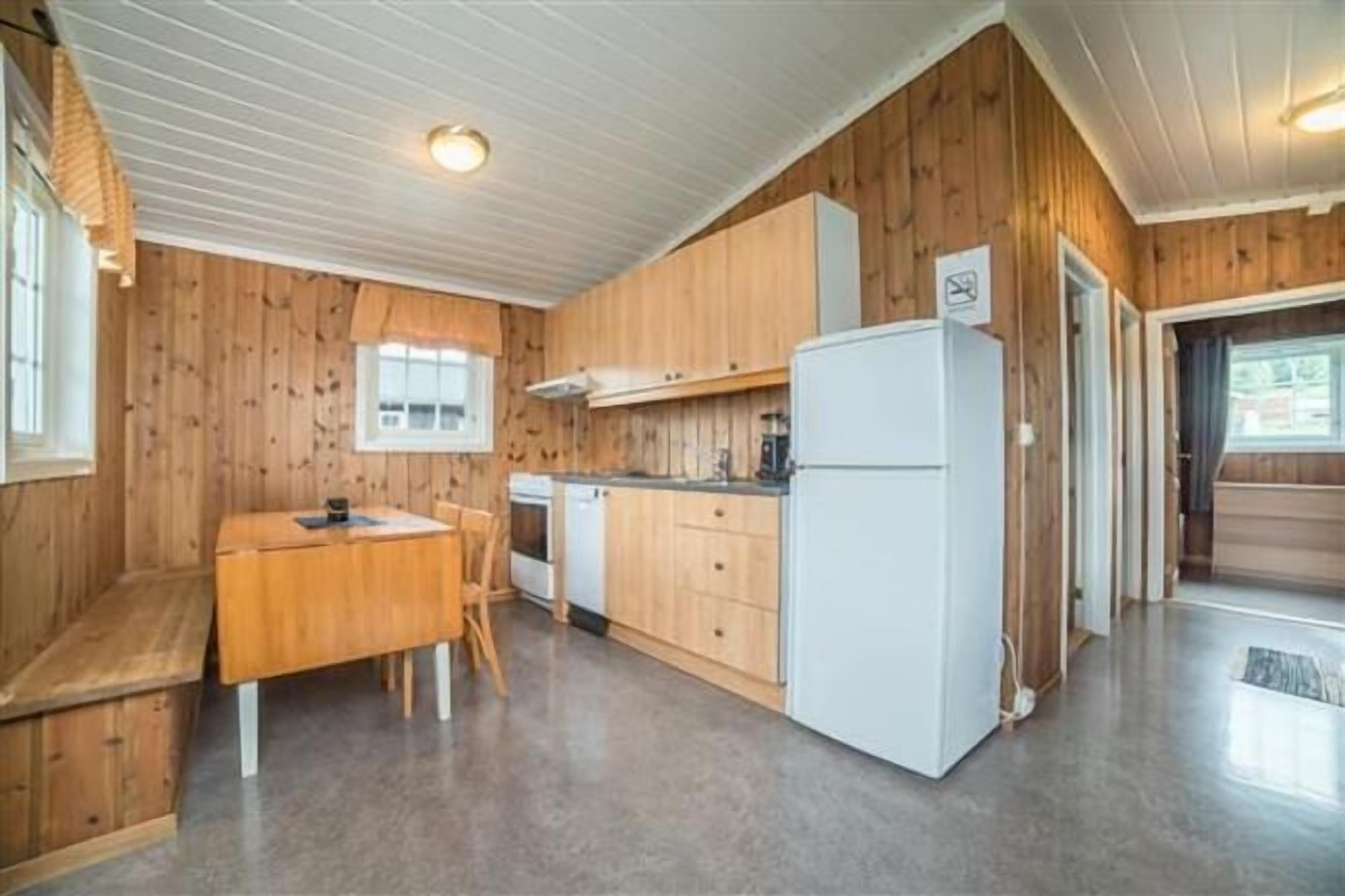 Eine kleine Küche mit Holzwänden, einem weißen Kühlschrank, einem Herd und einem Esstisch mit Stühlen.
