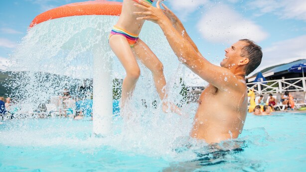 A man and a child playing in a water fountain at a pool. - Pluscamp Mageli  (Øyer)