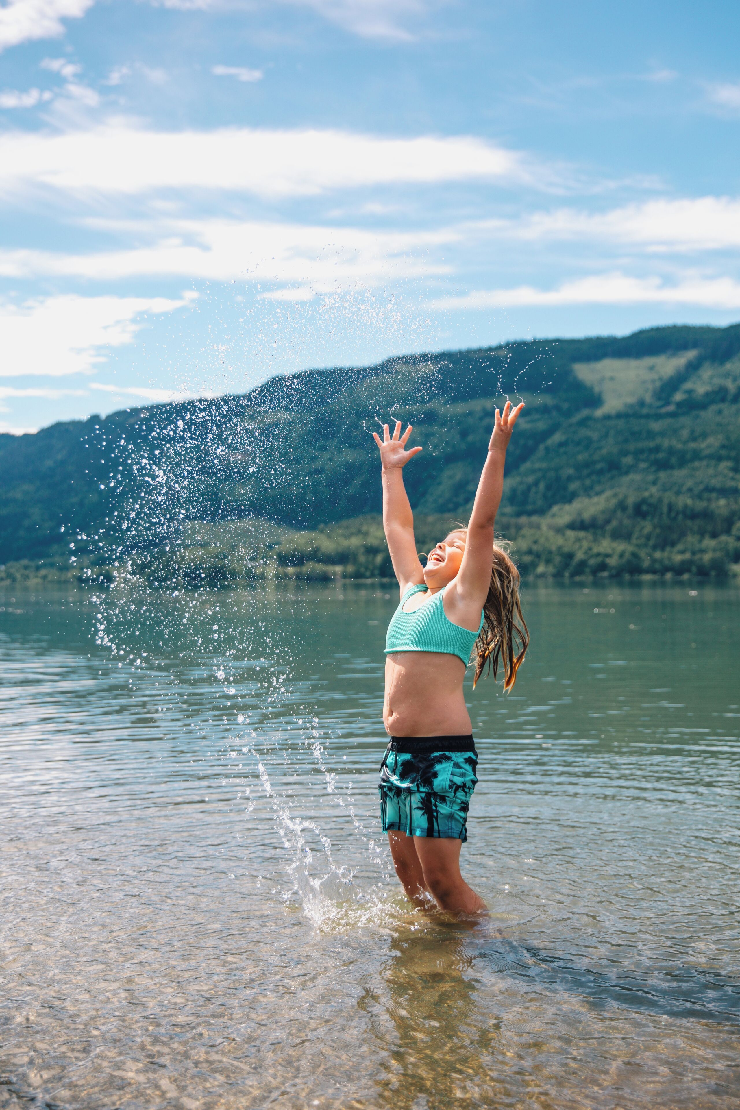 A person standing in shallow water with arms raised, splashing water.