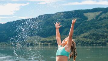 A person standing in shallow water with arms raised, splashing water.