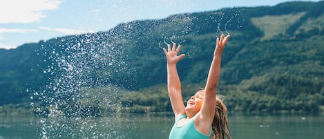 A person standing in shallow water with arms raised, splashing water.
