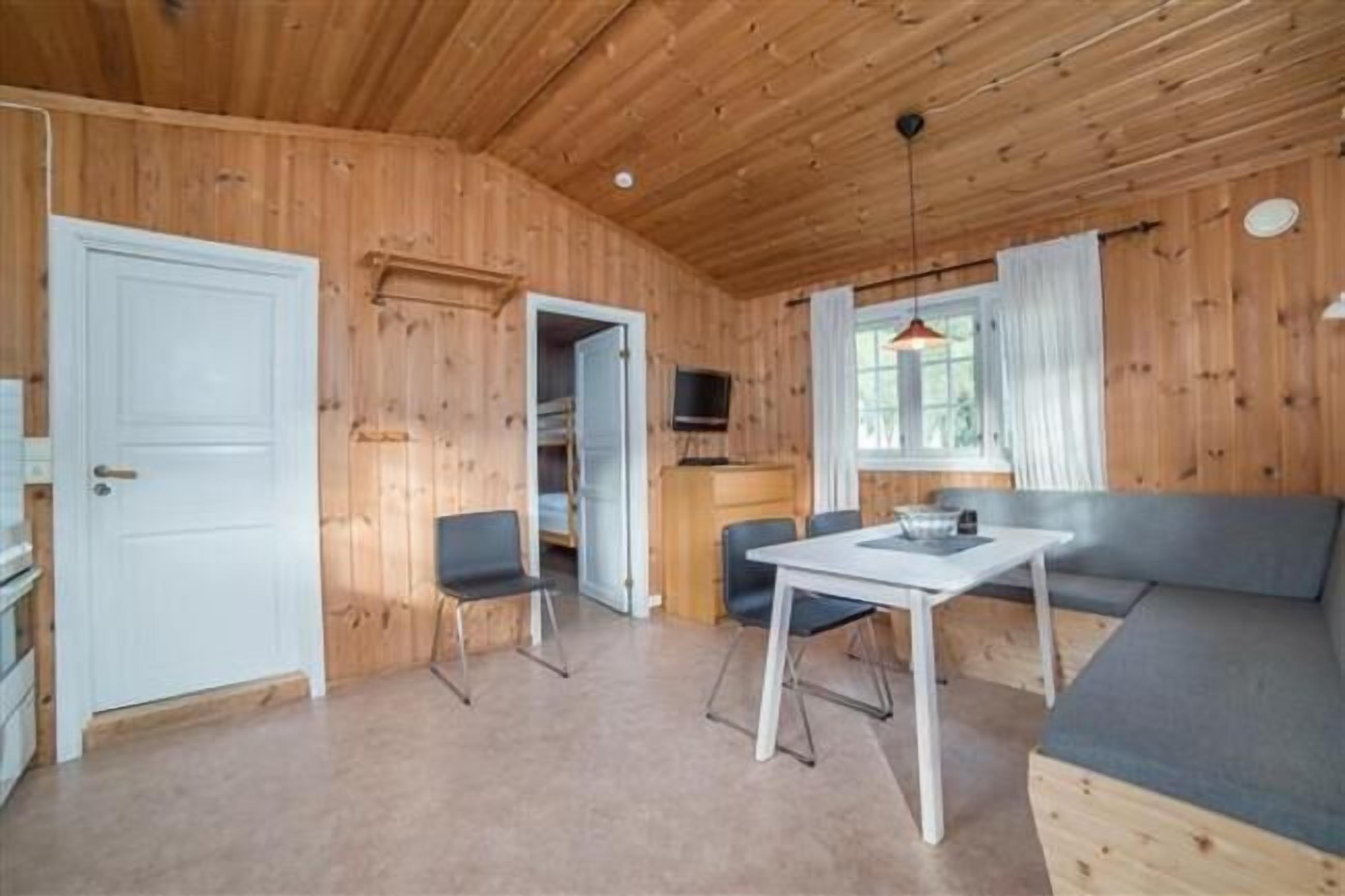 A wooden cabin interior with a dining table, chairs, a sofa, and a television.