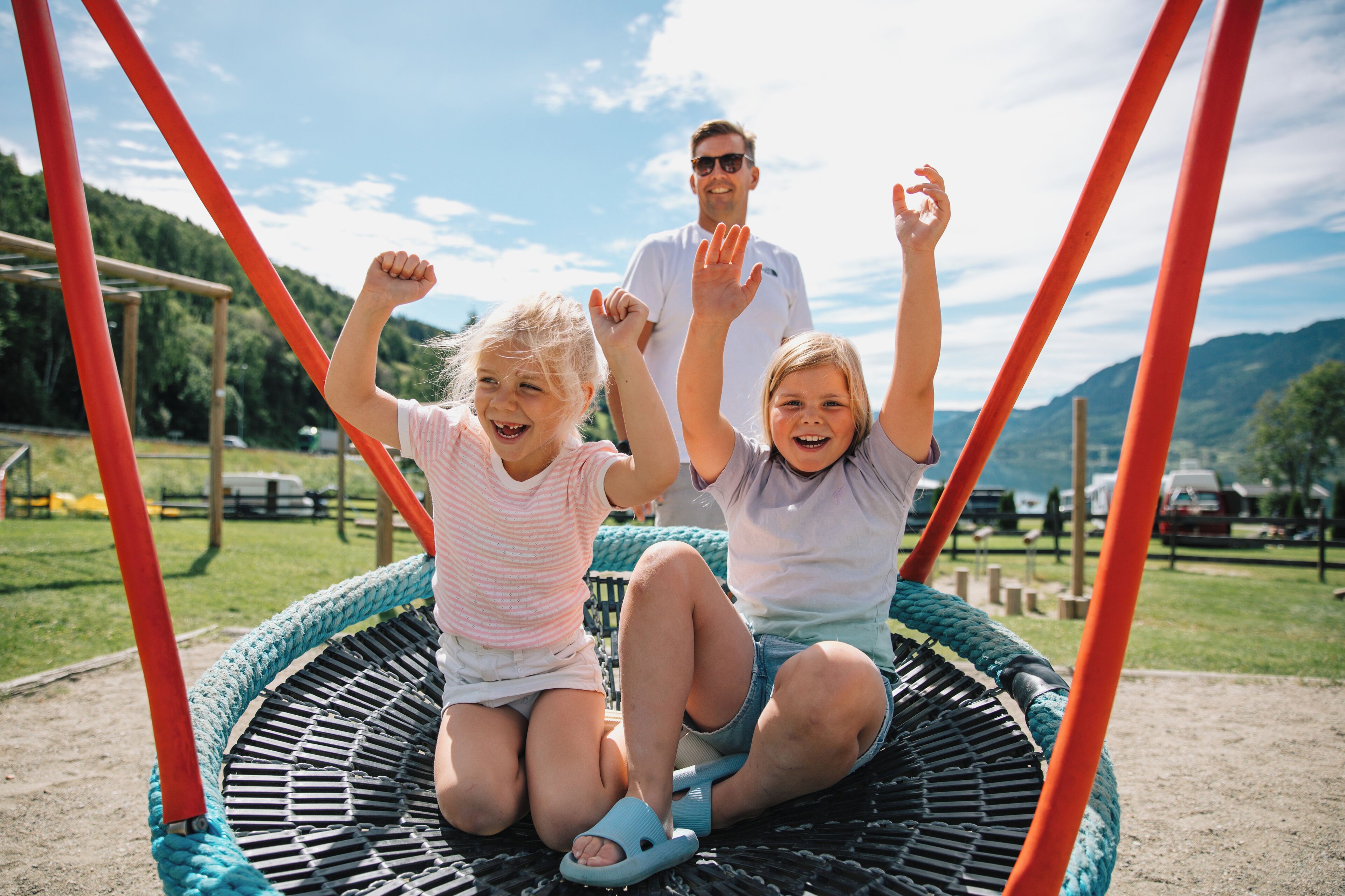 A family on a swing set with a mountainous backdrop.