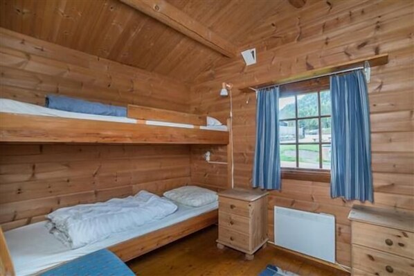 A wooden cabin room with bunk beds, a small dresser, a desk, and a window with curtains. - Pluscamp Mageli (Øyer)