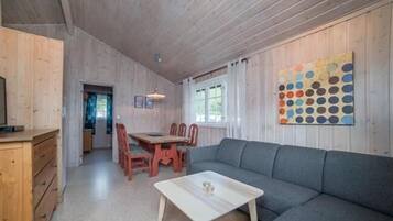 A cozy room with a wooden ceiling, a gray sofa, a wooden dining table with chairs, and a colorful wall art piece.