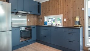 A modern kitchen with blue cabinets, stainless steel appliances, and a wooden wall paneling. - Pluscamp Mageli  (Øyer)