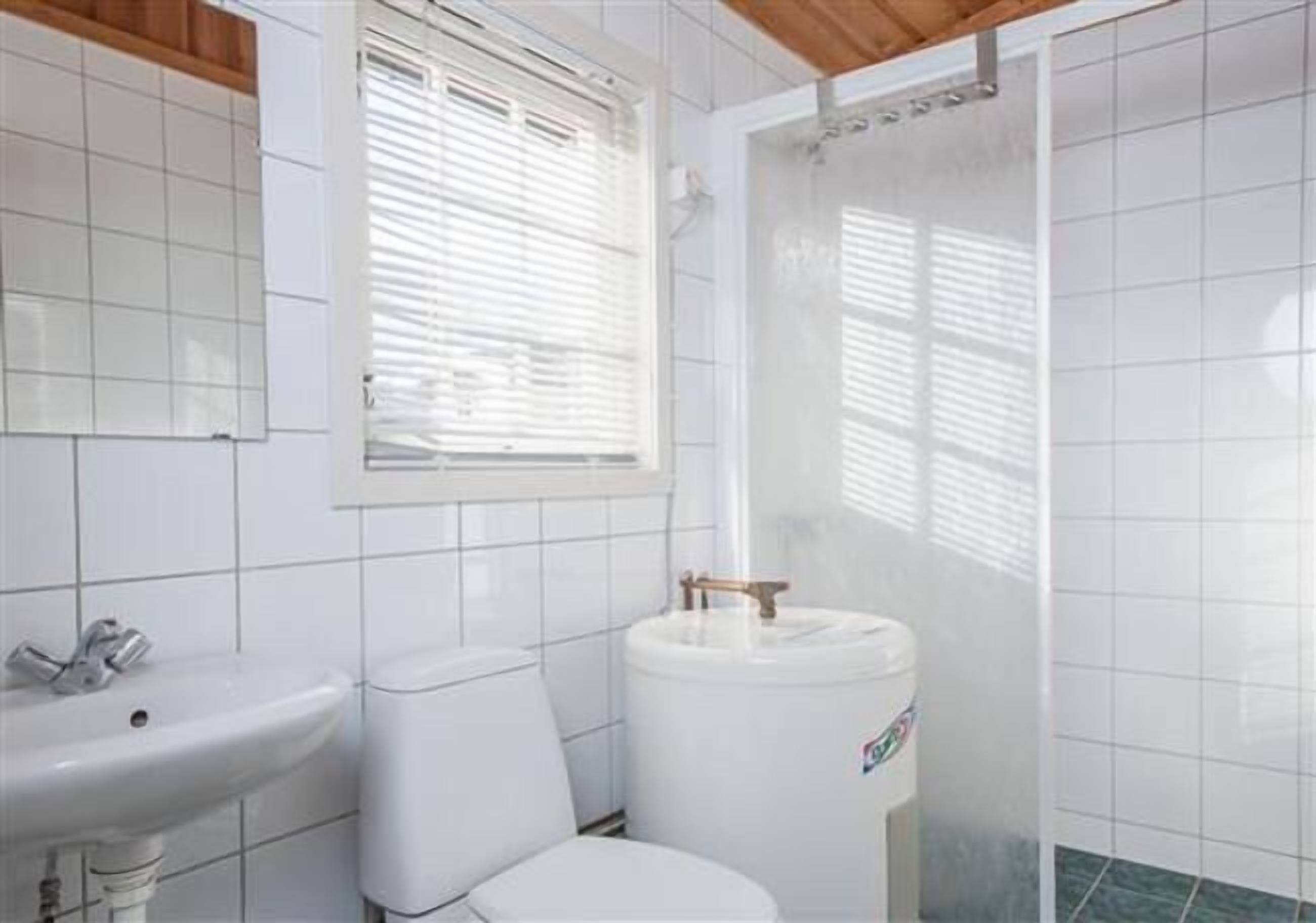 A bathroom with white tiles, a sink, a toilet, and a water tank.