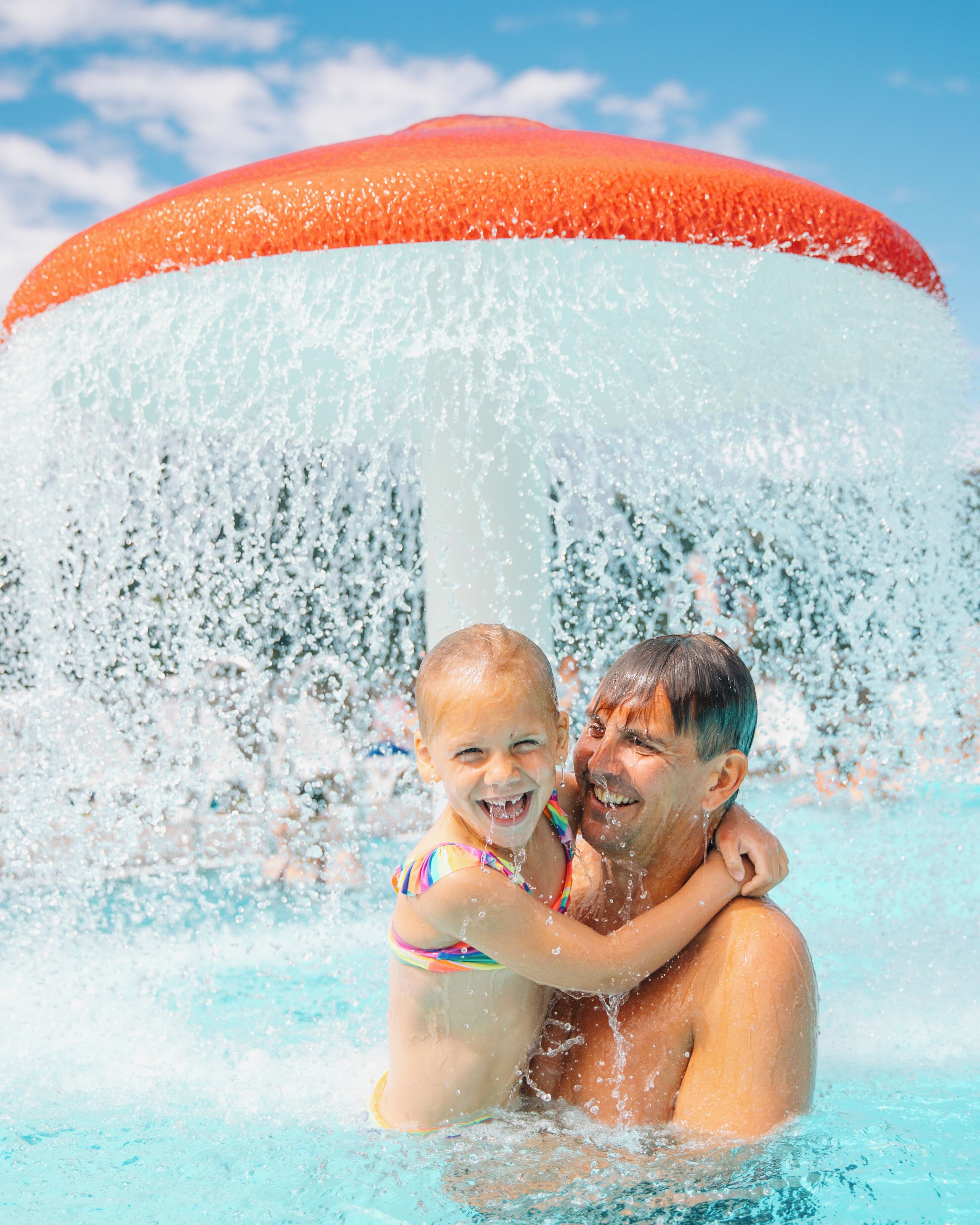 A water play area with a large water fountain and a person holding a child.