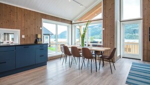A modern kitchen with wooden paneling, a dining area with a table and chairs, and large windows offering a view of the outdoors. - Pluscamp Mageli  (Øyer)