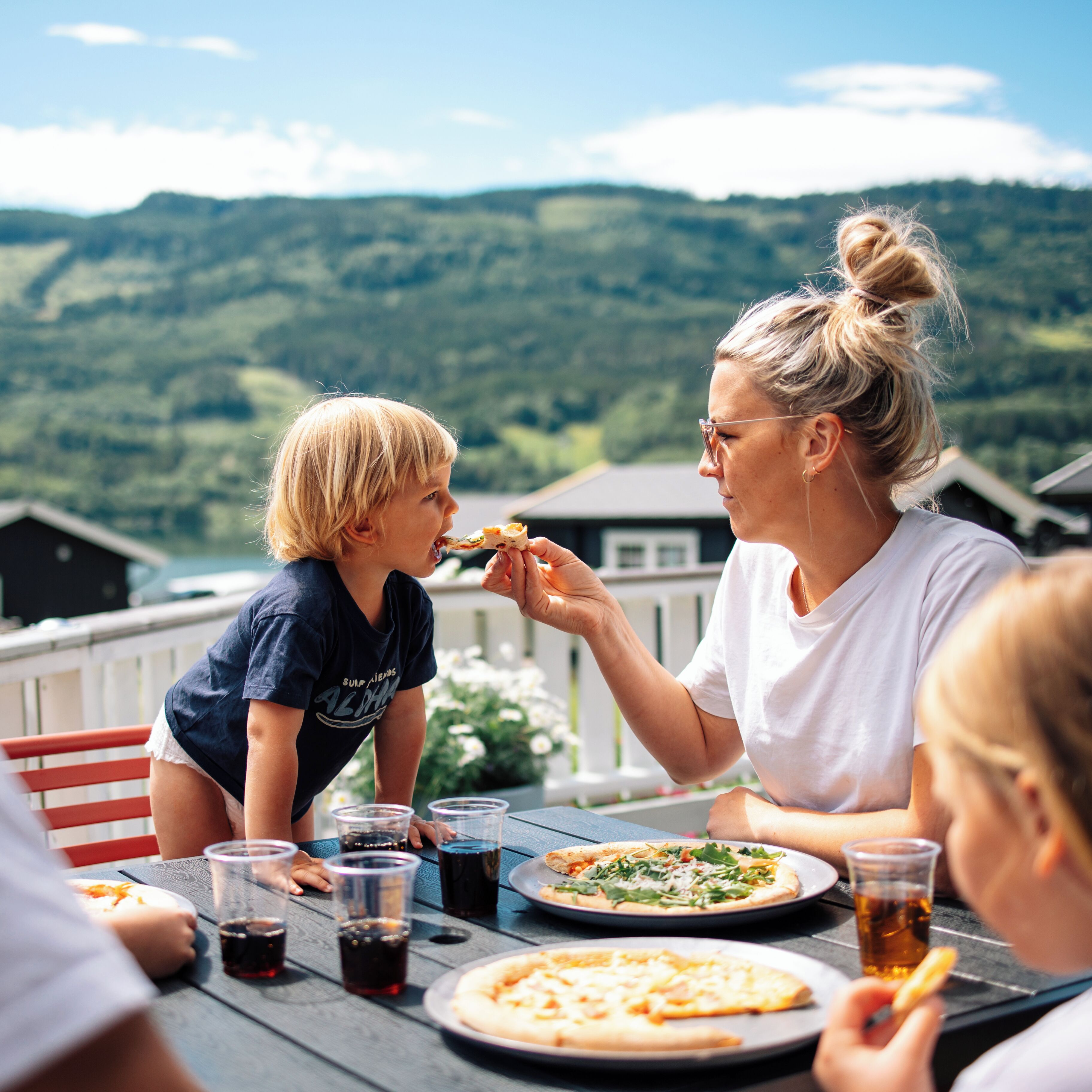 Ein Esstisch mit Pizza und Getränken vor einer Berglandschaft.