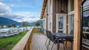 A wooden deck with a table and chairs, overlooking a lake and mountains. - Pluscamp Mageli  (Øyer)